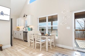 A modern kitchen with white cabinetry, a dining area with two chairs, and a large window with blinds.