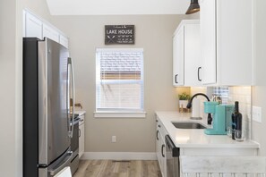 A modern kitchen with white cabinets, a stainless steel refrigerator, a window with blinds, and a sign reading "Welcome to the Lake House." - Private Hot Tub, Free Tickets, Near Silver Dollar City & Community Indoor Pool (Kimberling City)