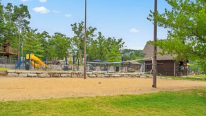 Un parque infantil con tobogán y estructuras para escalar, rodeado por una valla y árboles.