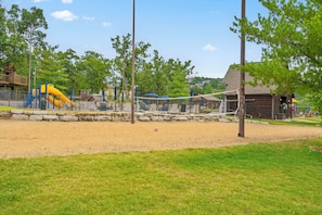 A playground with a slide and climbing structures, surrounded by a fence and trees. - On Table Rock Shoreline w/ Lake Views, Private Hot Tub, Billiards, Boat Slip & Cmty Amenities (Branson)