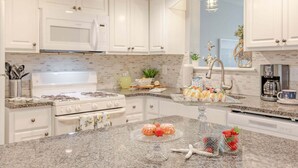 Une cuisine avec des meubles blancs, un plan de travail en granit, une cuisinière et une machine à café.