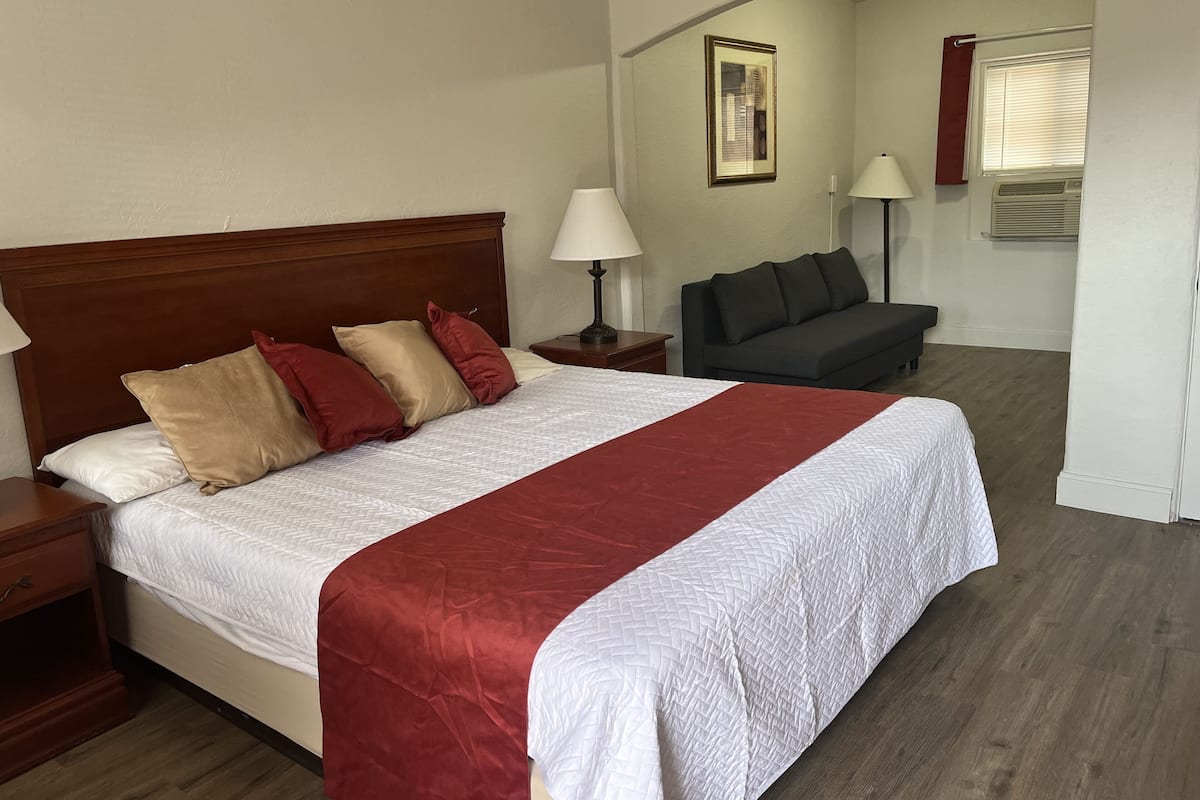 A hotel room with a bed, a sofa, a lamp, and a picture on the wall.