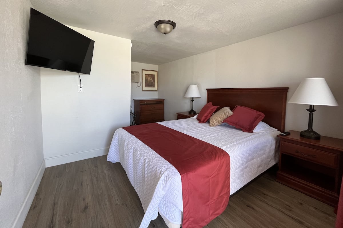 A hotel room with a bed, two bedside tables, a TV mounted on the wall, and a ceiling light.
