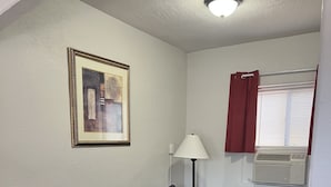 A room with a dark grey sofa, a framed picture on the wall, a floor lamp, a window with red curtains, and a ceiling light. - Arizona 9 Motor Hotel  (Williams)