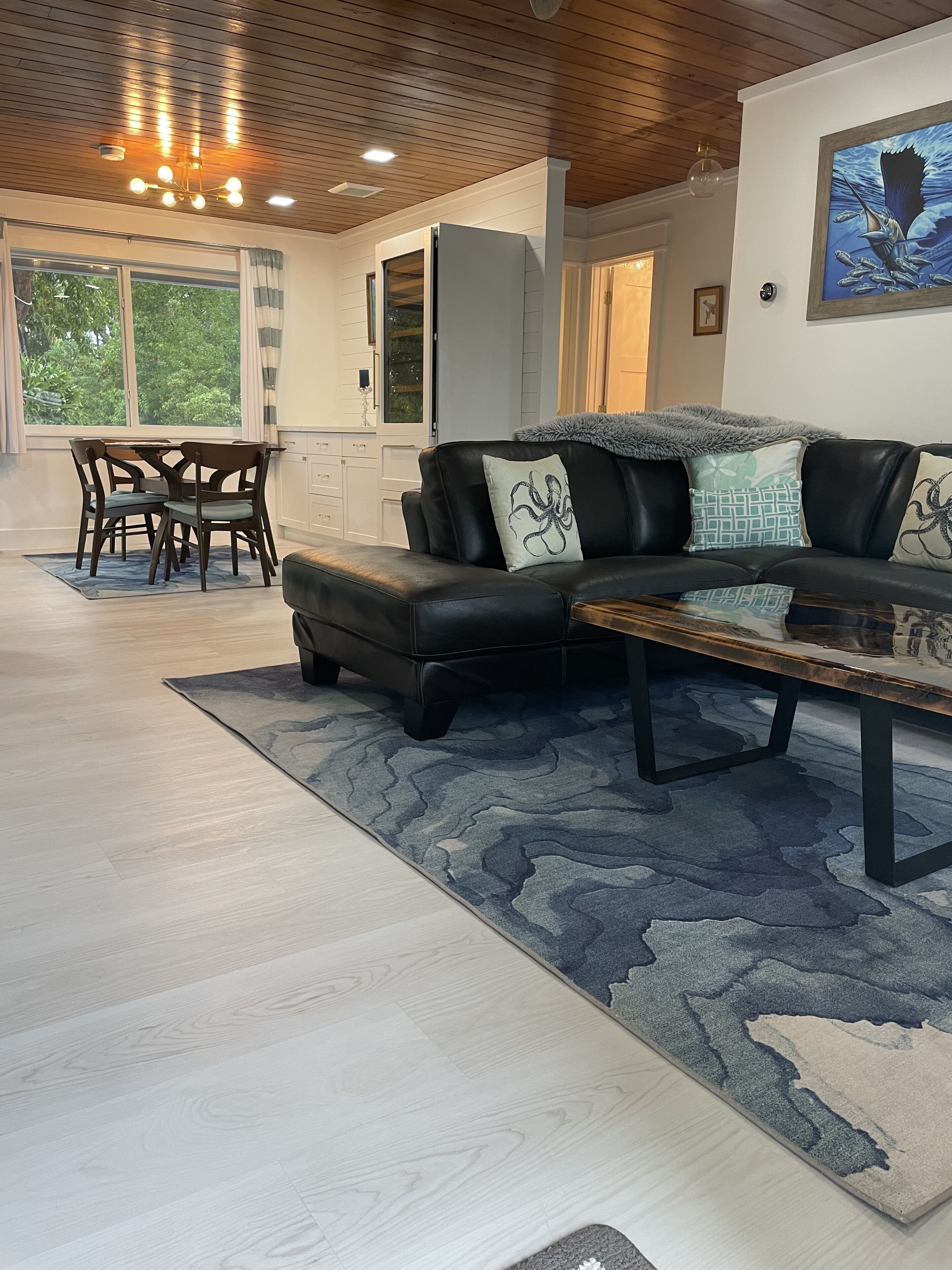 A spacious living room with a black leather sofa, a glass coffee table, and a dining area with wooden chairs and a table.