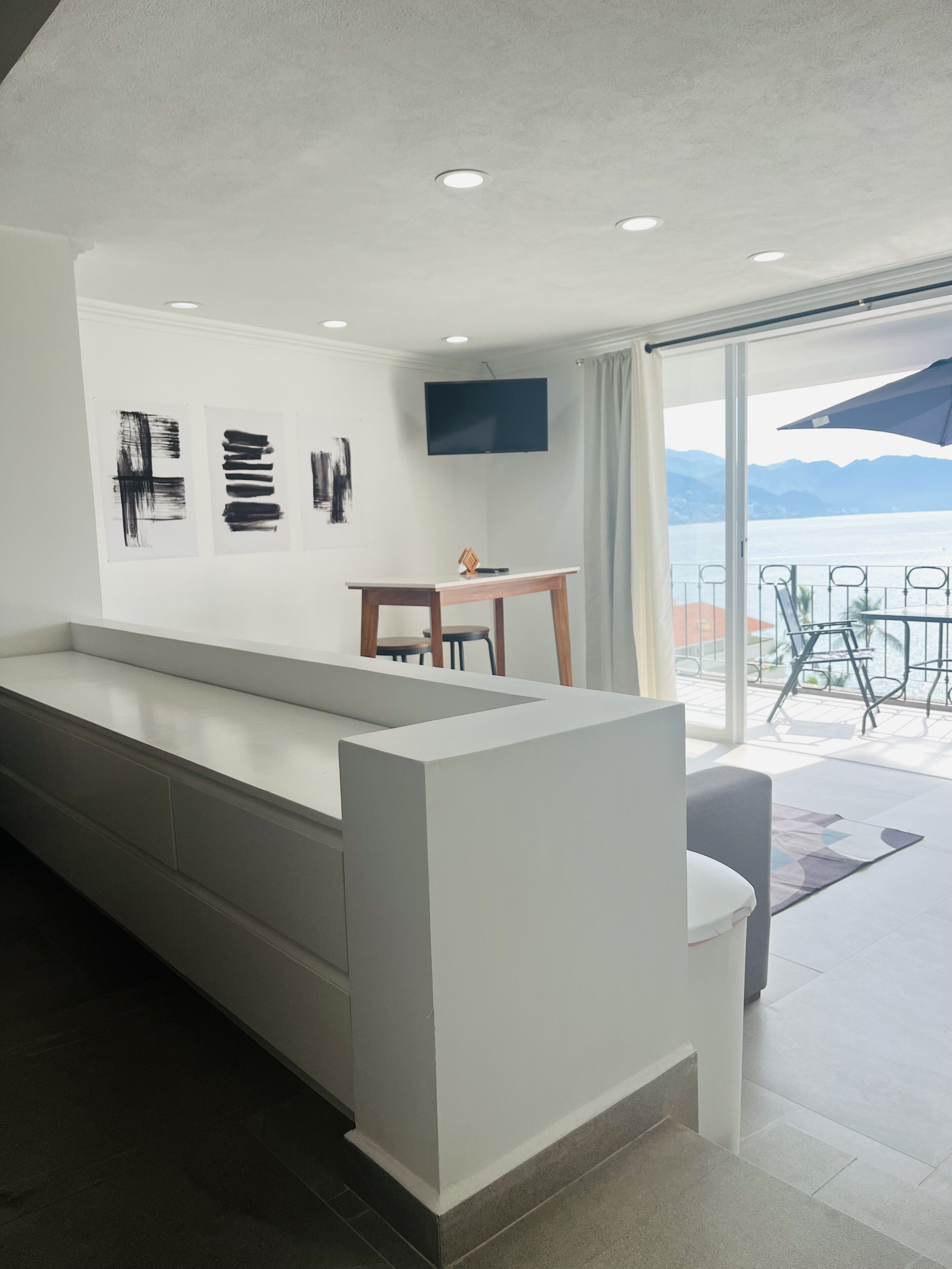 A modern kitchen with a long island counter, a dining area with a table and chairs, and a TV mounted on the wall.