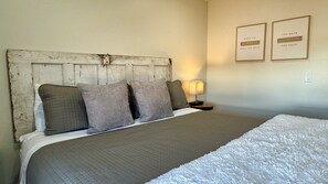 A bedroom with a rustic wooden headboard, a bed with grey bedding, a white throw, and two framed inspirational quotes on the wall.