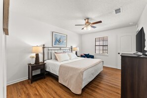 Ein Schlafzimmer mit einem Bett, Nachttischen, einem Deckenventilator, einem Fenster mit Jalousien und einem Fernseher.