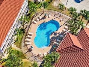 Luftaufnahme eines Resorts mit einem zentral gelegenen Schwimmbad, umgeben von Liegestühlen und Palmen.