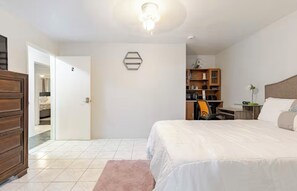 Une chambre à coucher comprenant un lit, un bureau, une armoire et une porte donnant sur une autre pièce.