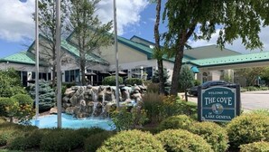 A hotel entrance with a sign reading "Welcome to The Cove of Lake Geneva," a landscaped garden with a water feature, and a building with a green roof.