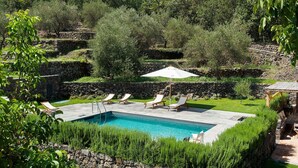 A swimming pool with lounge chairs and an umbrella, surrounded by stone walls and greenery.