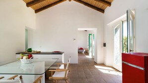A modern kitchen with a glass dining table, wooden chairs, a red refrigerator, and a view of the outdoors through a large window.