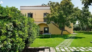 A two-story building with a yellow facade, a stone pathway leading to the entrance, and a well-maintained lawn.