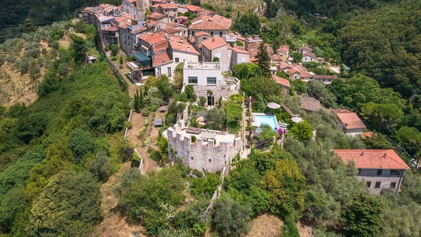 An aerial view of a hillside village with traditional stone buildings, a prominent church tower, and a swimming pool. - Stunning private villa with A/C, private pool, WIFI, TV, terrace, panoramic view, close to Viareggio (Camaiore)
