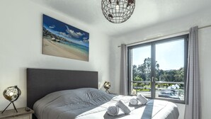 Une chambre avec un grand lit, une table de chevet, un globe terrestre et un tableau représentant une plage.