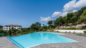 Une piscine avec une terrasse en bois, entourée de chaises longues et d’un bâtiment en arrière-plan.