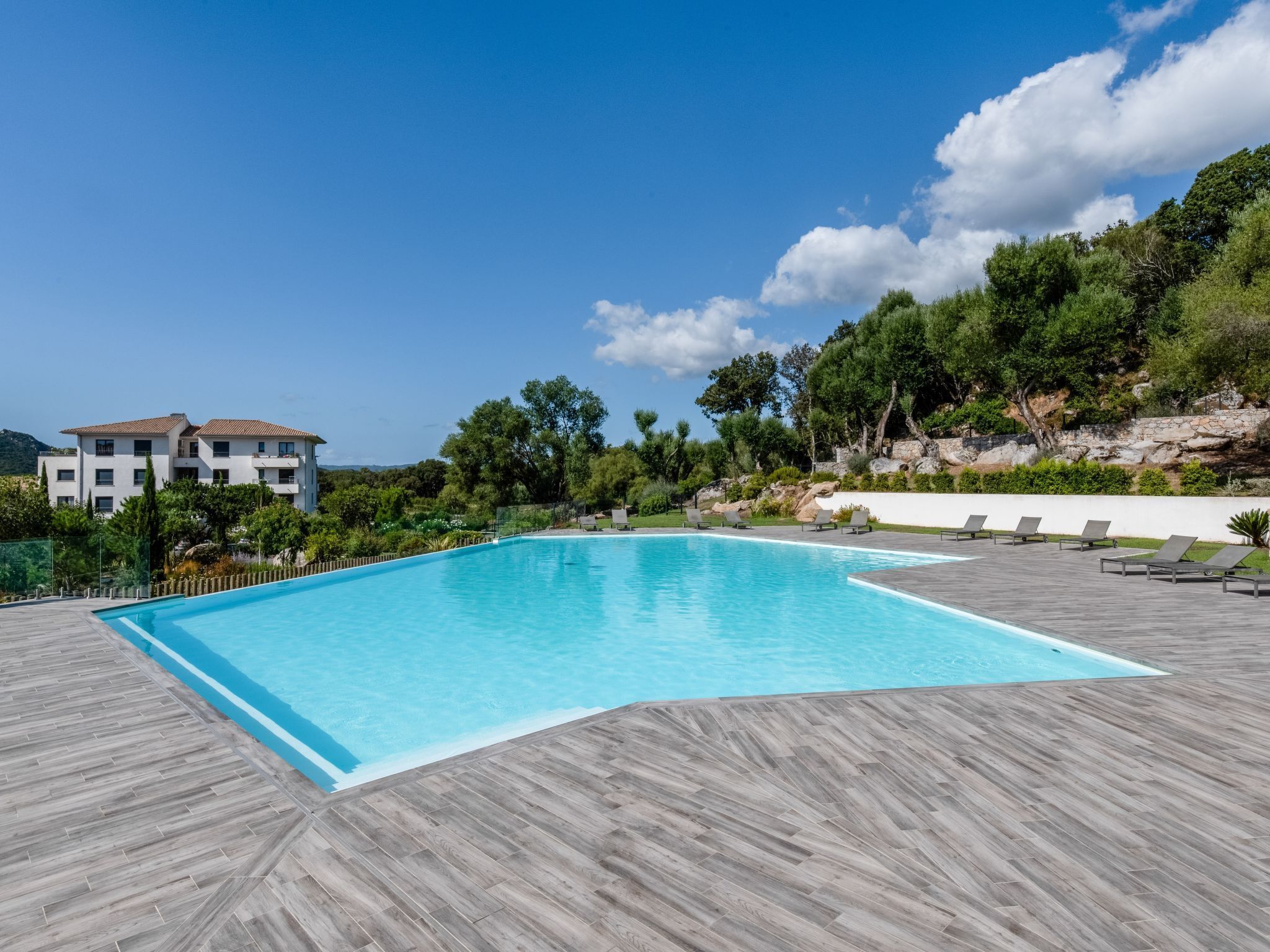 Una piscina con un pontile in legno, circondata da lettini e un edificio sullo sfondo.