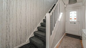 Una escalera con barandilla blanca, una puerta con un ventanal floral y una alfombra gris.
