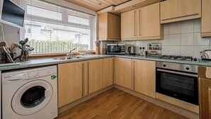 Cocina compacta con armarios de madera, microondas integrado, cocina a gas y lavadora.