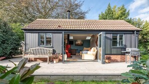 A cozy cottage with a tiled roof, a wooden deck, and a patio area with a bench and a sofa. - The Little House, Orford (Orford)