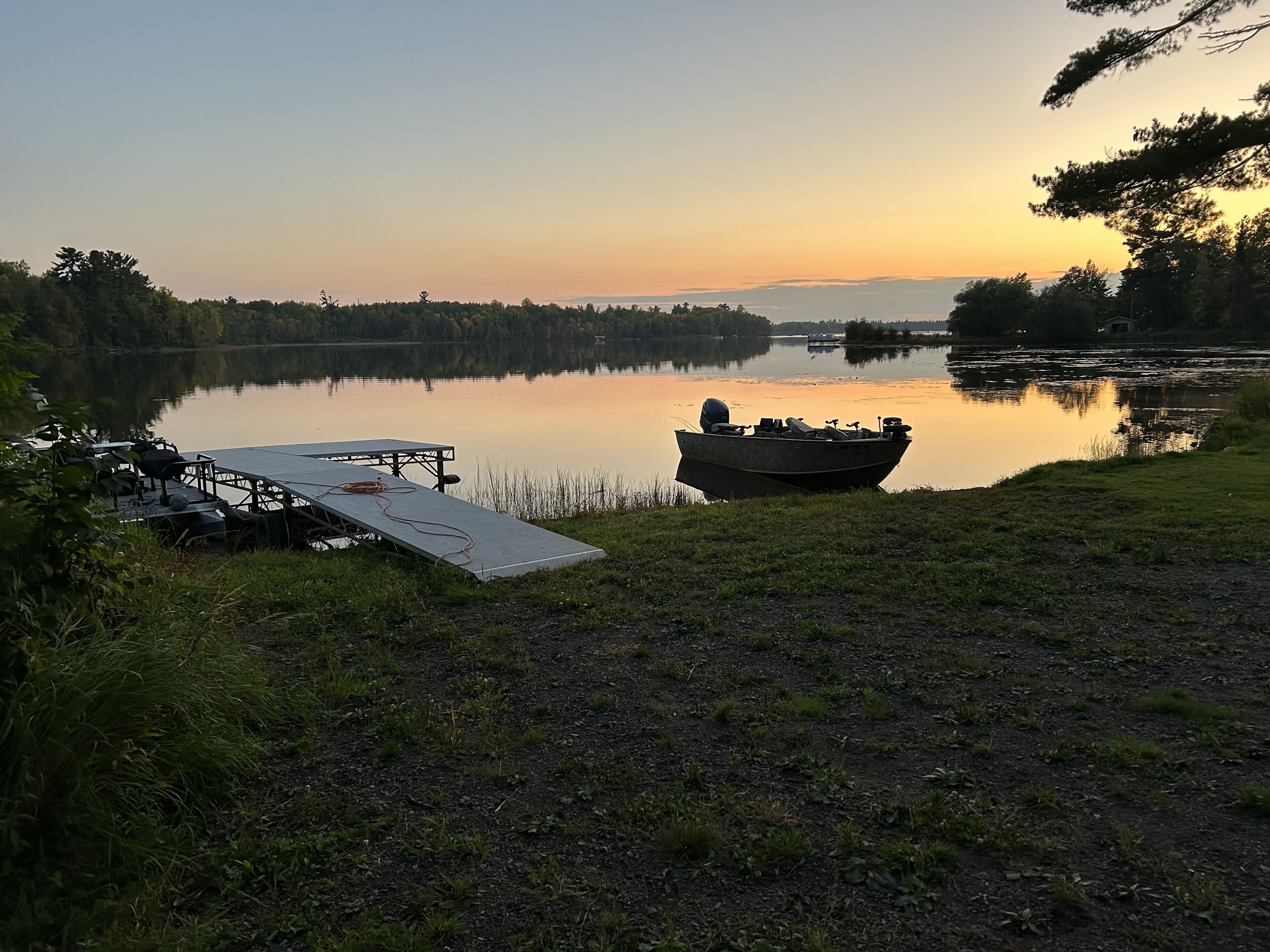 A calm lake at sunset with a dock and a boat.