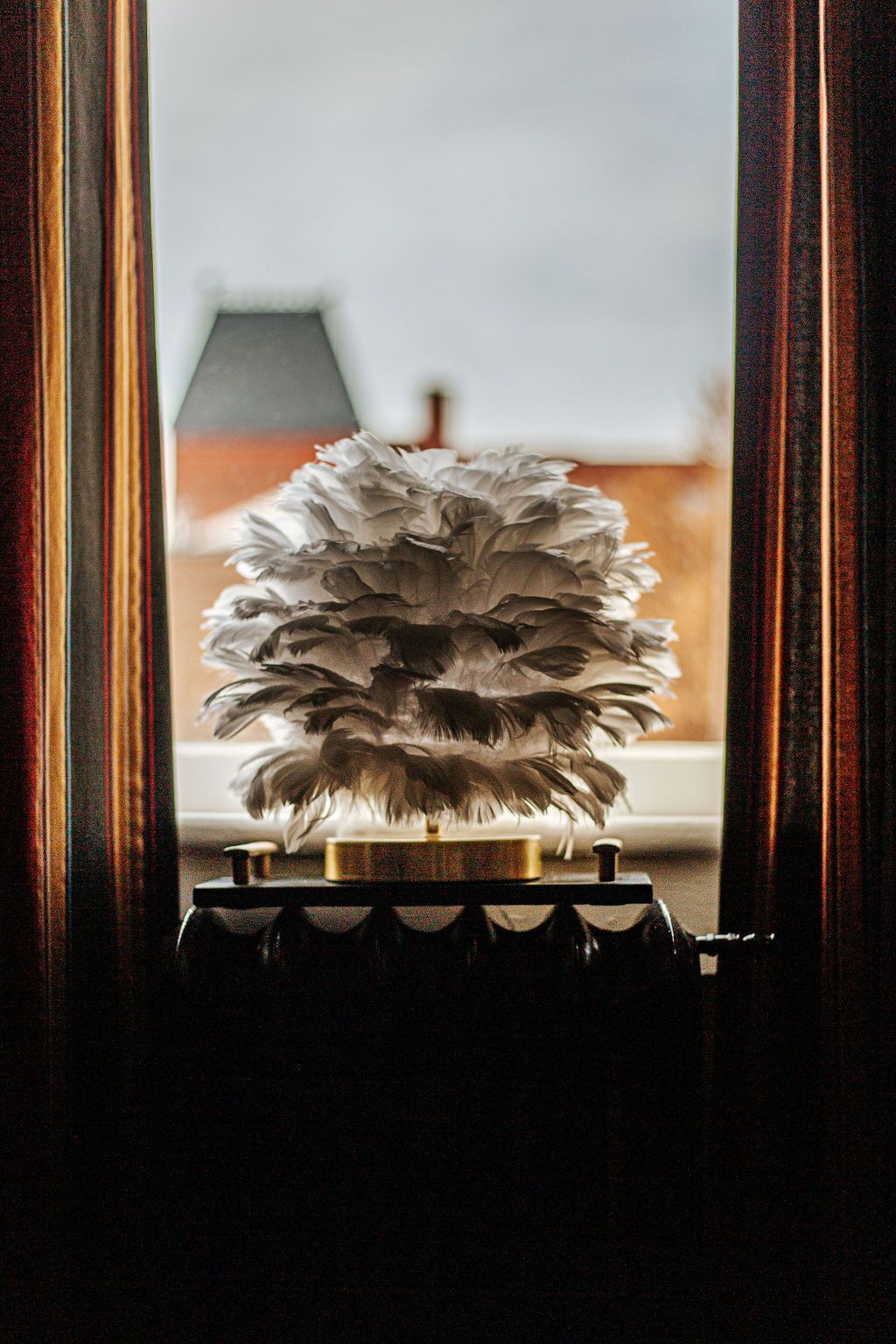 Een decoratief object met veren voor een raam met uitzicht op gebouwen.