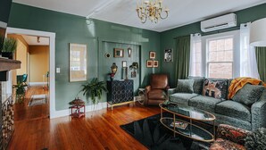 Een woonkamer met een groene wand, een bruine leren fauteuil, een groene bank, een glazen salontafel en een kroonluchter.