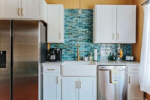 A kitchen with white cabinets, a stainless steel refrigerator, a coffee maker, and a dishwashing machine.