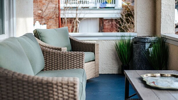Een rieten bank met kussens, een houten tafel en een blauw vloerkleed in een gezellig zitgedeelte buiten.