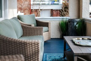 A wicker sofa with cushions, a wooden table, and a blue rug in a cozy outdoor seating area.