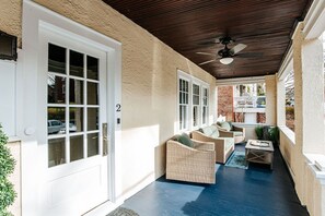 Une terrasse couverte, aménagée avec des meubles en osier et dotée d’un ventilateur de plafond.