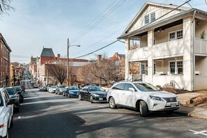 Une vue de rue avec des voitures garées, un immeuble doté d’un balcon et un ciel dégagé.