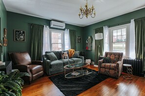 Ein Wohnzimmer mit grüner Wand, einem braunen Ledersessel, einem gemusterten Sessel, einer grünen Couch, einem Couchtisch und einer Chandelier.