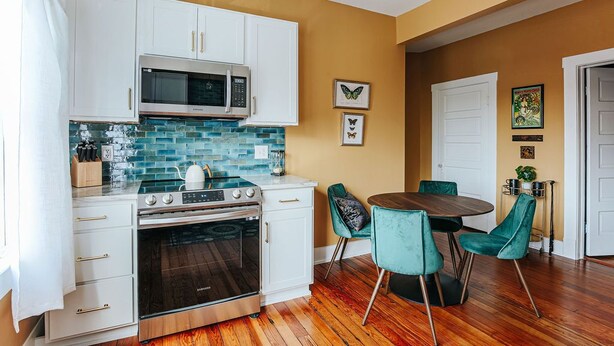 A kitchen with white cabinets, a microwave, a stove, and a dining area with teal chairs.