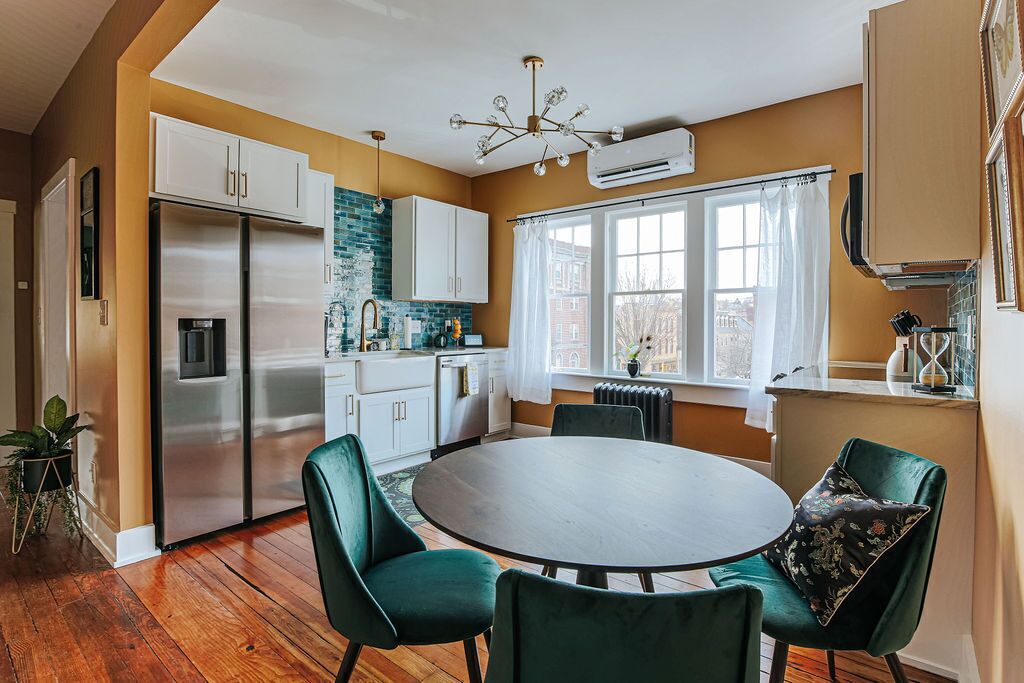 A modern kitchen with a dining area, featuring a stainless steel refrigerator, white cabinets, a round dining table, and green chairs.