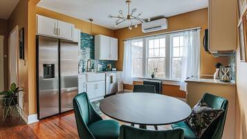 A modern kitchen with a dining area, featuring a stainless steel refrigerator, white cabinets, a round dining table, and green chairs.