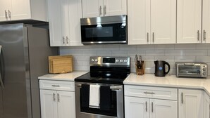 Une cuisine moderne avec des meubles blancs, des appareils en acier inoxydable, notamment un réfrigérateur, un four à micro-ondes et un four traditionnel, ainsi qu’un grille-pain.