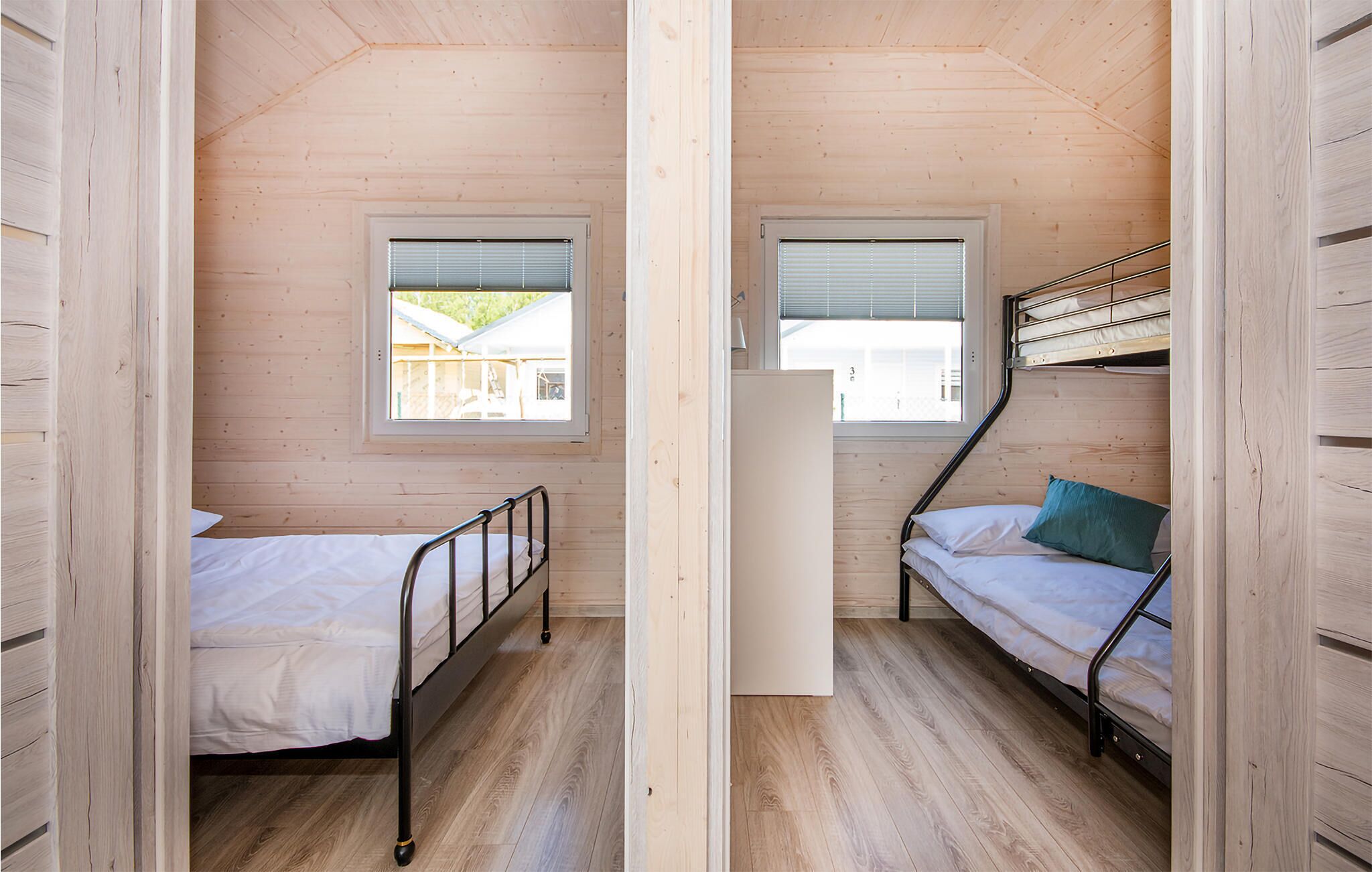 A compact room with two bunk beds and a window, wooden walls, and a sloped ceiling.