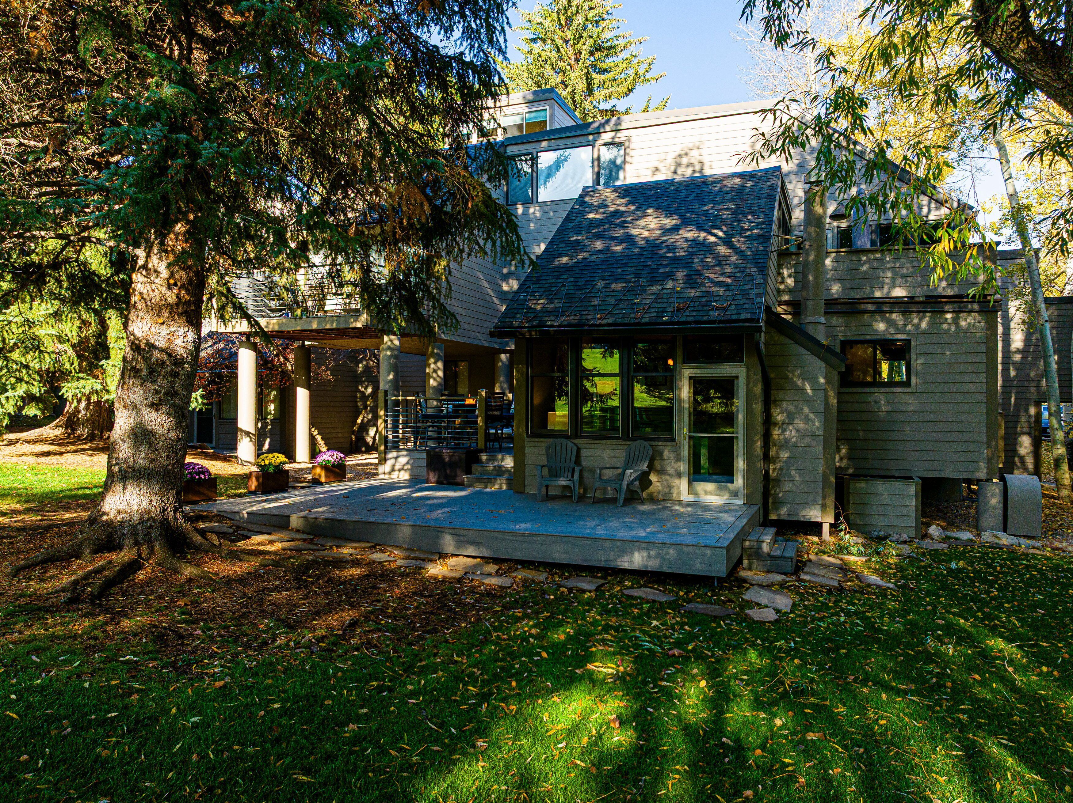 A house with a covered porch, a small deck, and a large tree in the foreground.