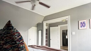 A bedroom with a bed, a ceiling fan, a door leading to another room, and a wall with framed pictures. - Birthday Suite / 1 BD/1BA Apt in Holiday House (Evansville)