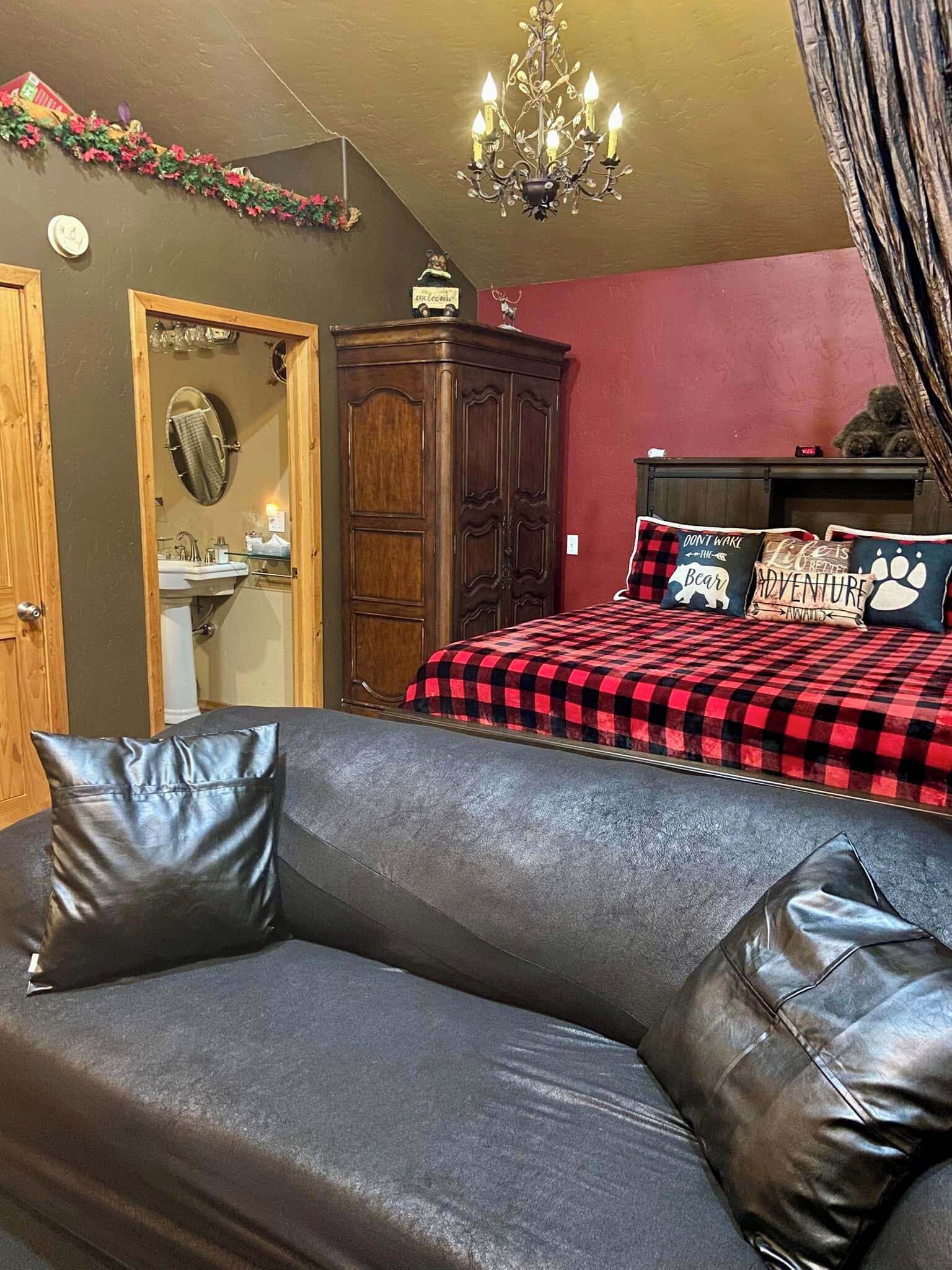 Une chambre à coucher avec une couvre-lit à carreaux, une armoire en bois, un miroir, un lustre et un canapé en cuir.