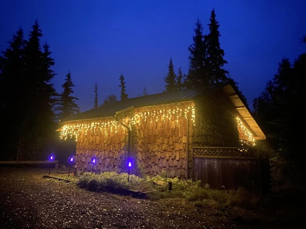 A rustic wooden cabin with string lights and purple lights on the ground. - Bear Cabin-Gunning Cabin Rentals (Soldotna)