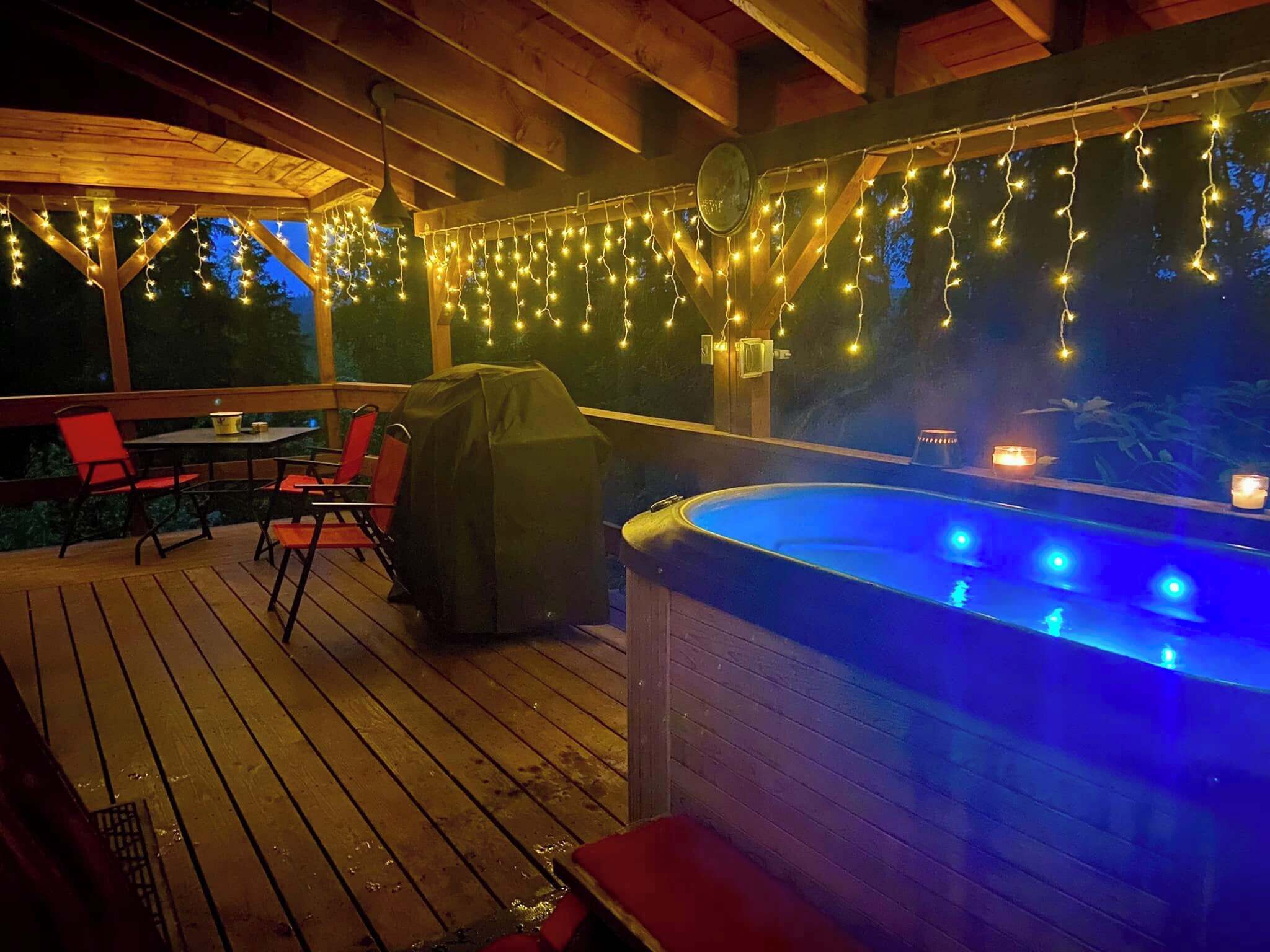 An outdoor deck with a hot tub, string lights, and a covered grill area.