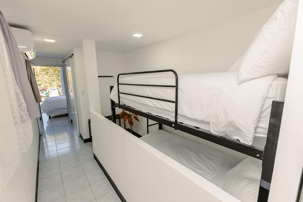 Une chambre avec un lit superposé, une fenêtre, une plante et un sol carrelé.