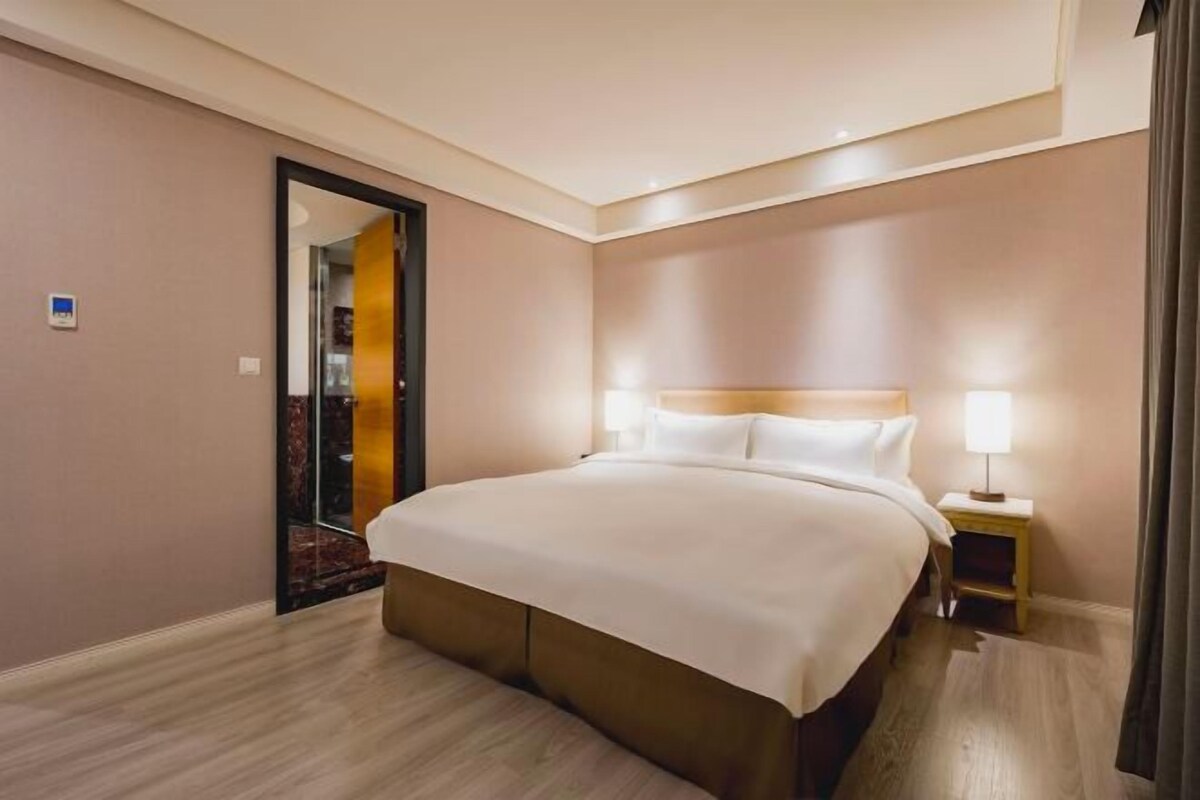 A hotel room with a large bed, a bedside table with a lamp, and a mirror on the wall.