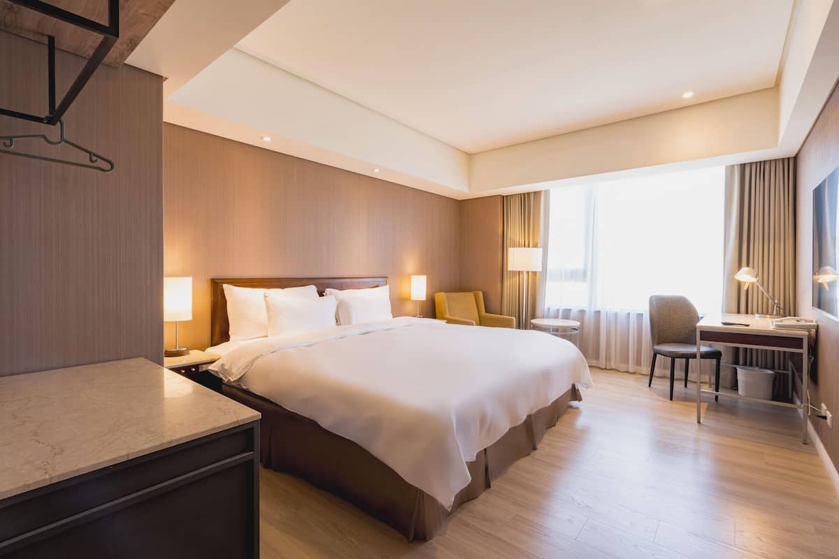A hotel room with a large bed, bedside tables, a desk with a chair, and a view of the outdoors.