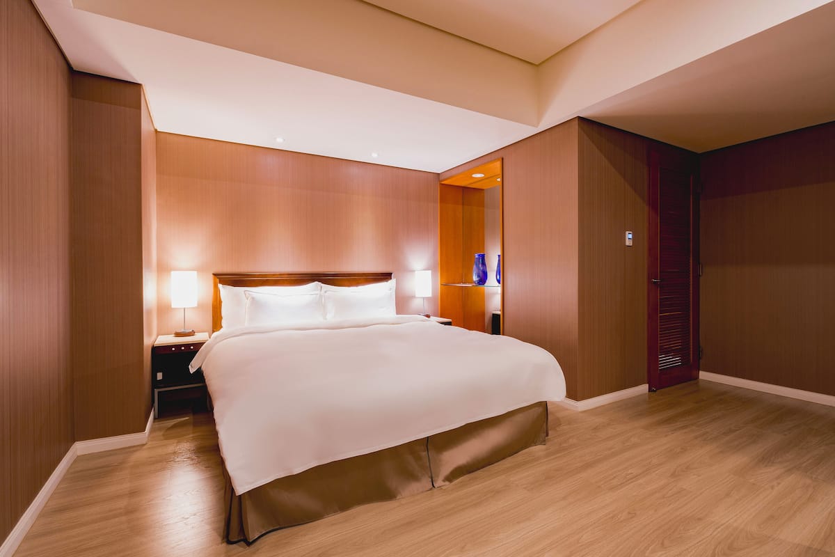 A hotel room with a large bed, wooden paneling, a nightstand with a lamp, and a wardrobe.