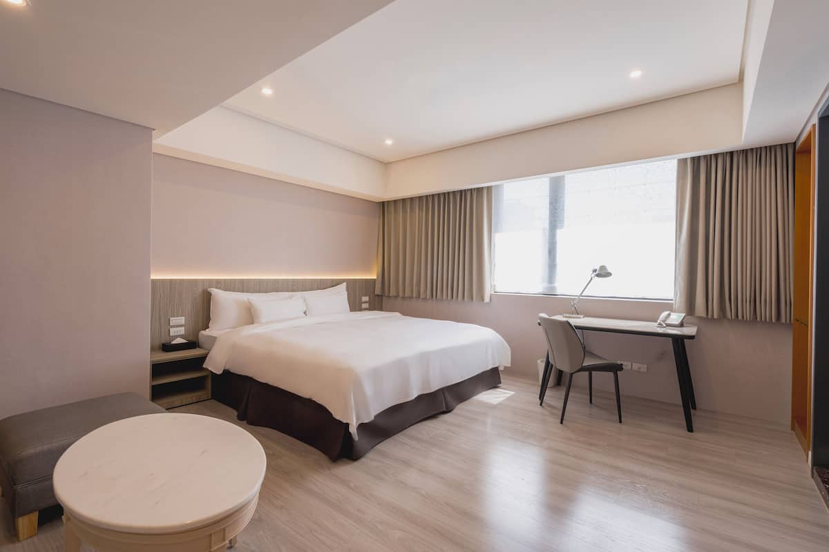 A modern hotel room with a large bed, a desk, and a chair.