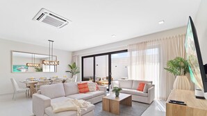A modern living room with a sofa set, a coffee table, a TV, and a dining area with a table and chairs. - 4BR Private Pool & Jacuzzi Boca Catalina Beach (Noord)